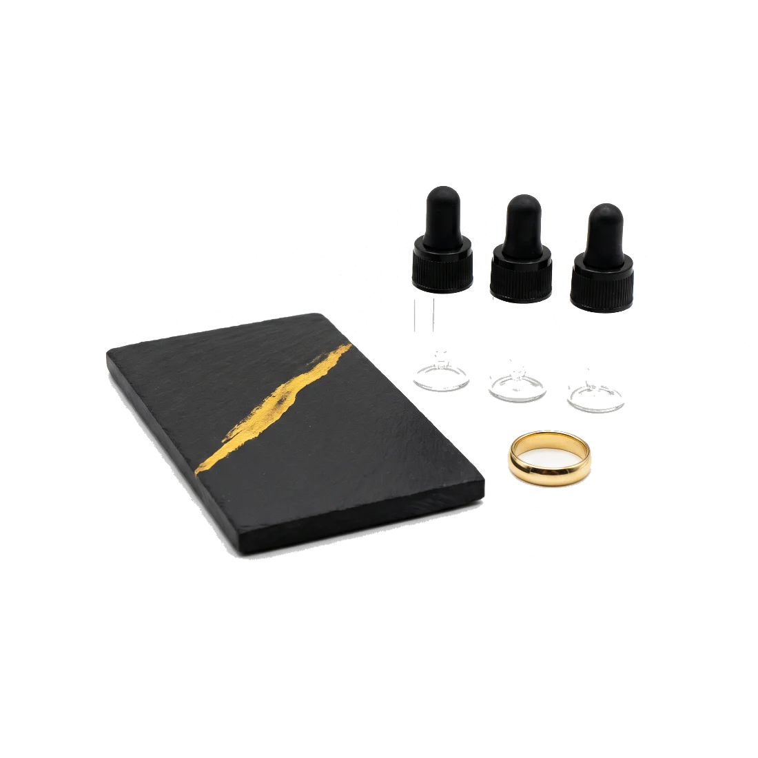 A black touchstone with a gold streak across it, beside three small capped dropper bottles and a gold ring.