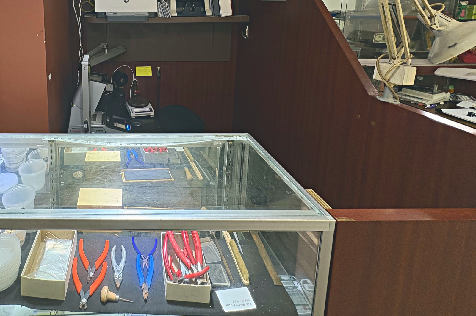 The working counter at Booth 57: a digital precision balance and testing instruments on the back bench, with pliers, cutters, files laid out inside the glass-topped case.