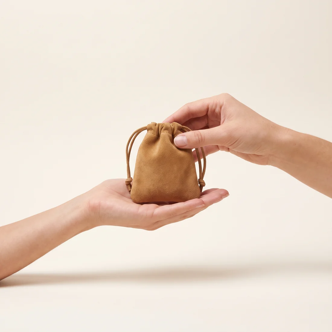 One hand passing a closed suede pouch into another open hand.