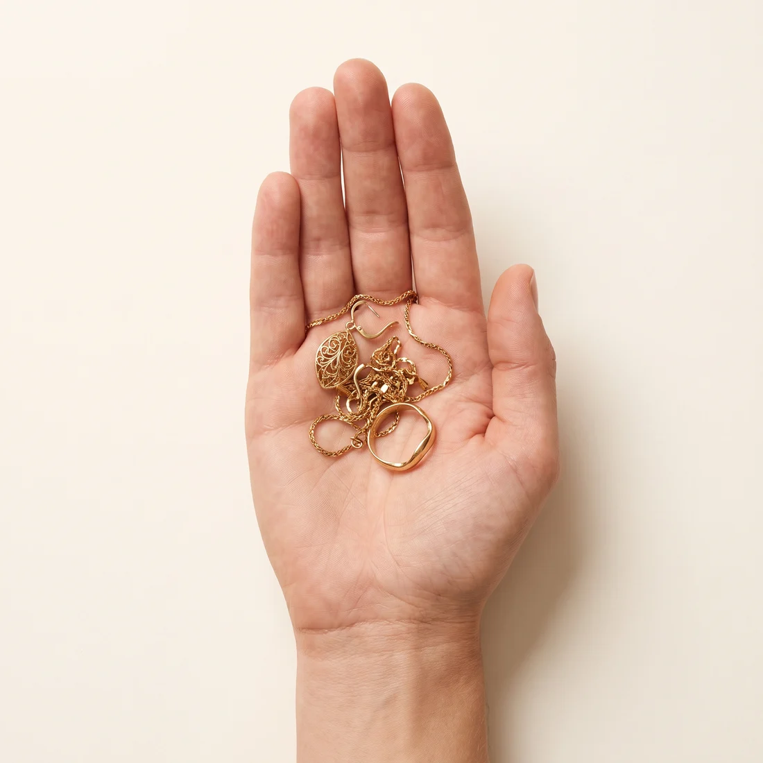 An open hand holding a small heap of broken gold jewellery.