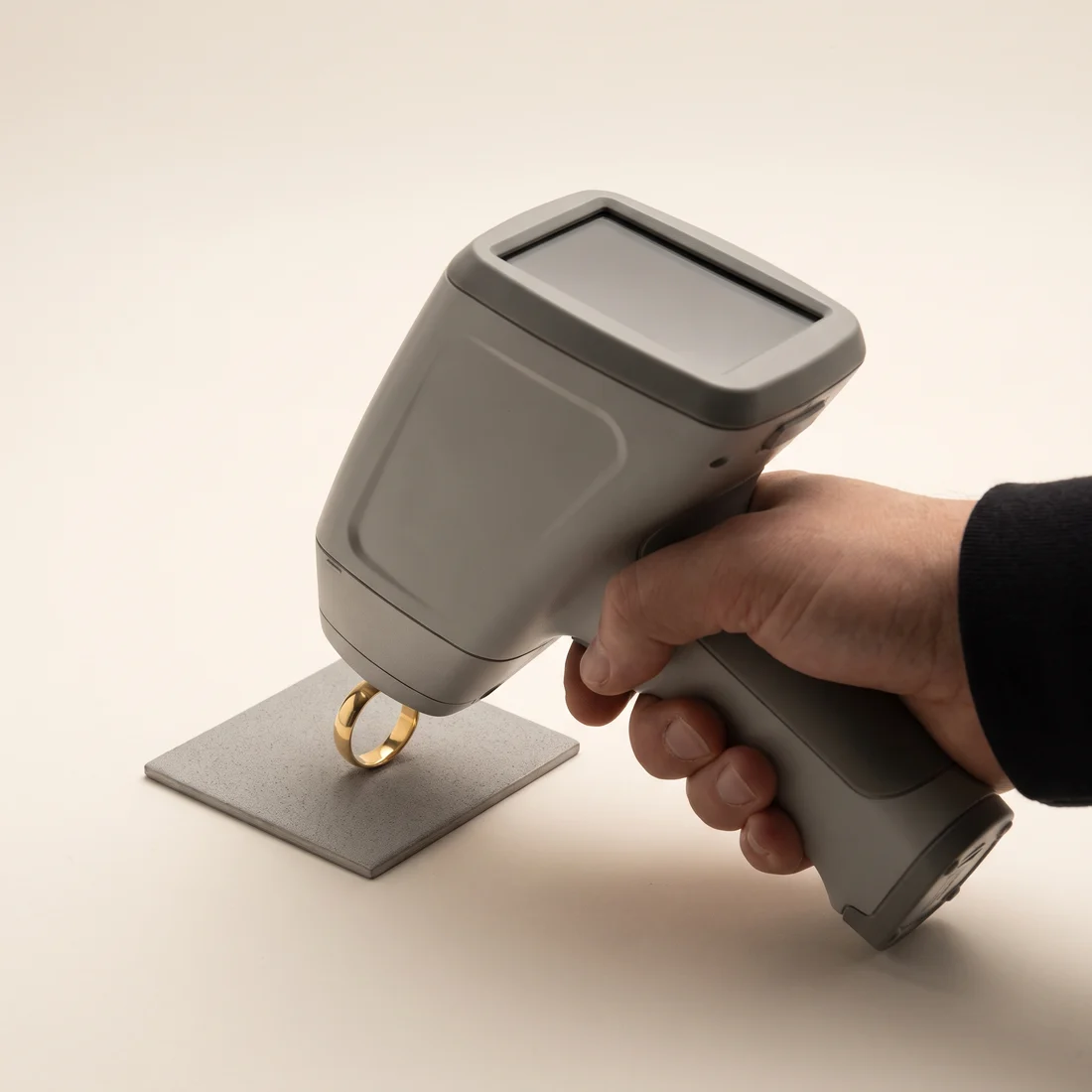 A handheld XRF analyser held against a plain gold ring on a test pad.